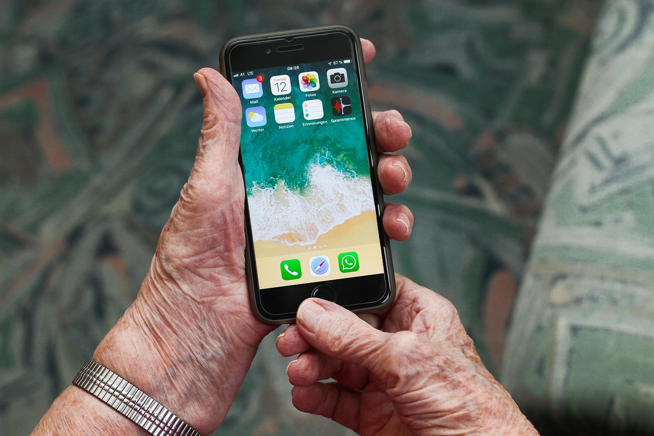 una manos de mujer mayor sujeta un teléfono móvil encendido en el que aparecen las aplicaciones de llamar, whatsapp, notas y correo electrónico