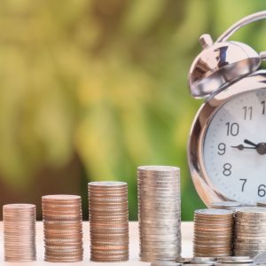 Reloj despertador junto a pilas de monedas simbolizando el ahorro para la jubilación.