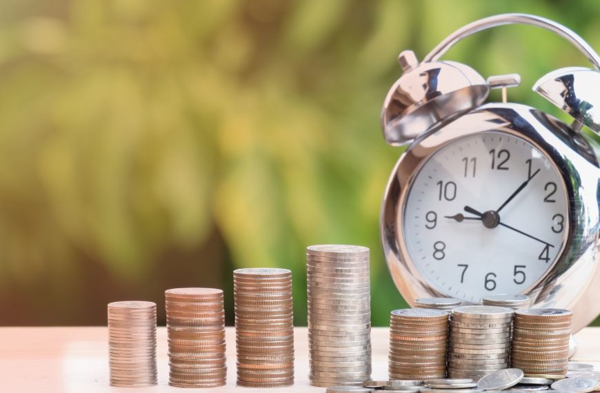 Reloj despertador junto a pilas de monedas simbolizando el ahorro para la jubilación.