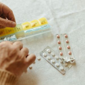 Persona organizando medicamentos en un pastillero semanal sobre una mesa.