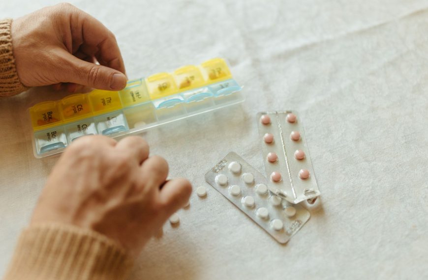 Persona organizando medicamentos en un pastillero semanal sobre una mesa.