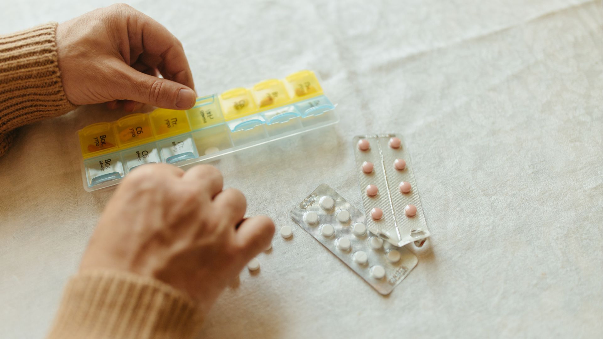 Persona organizando medicamentos en un pastillero semanal sobre una mesa.